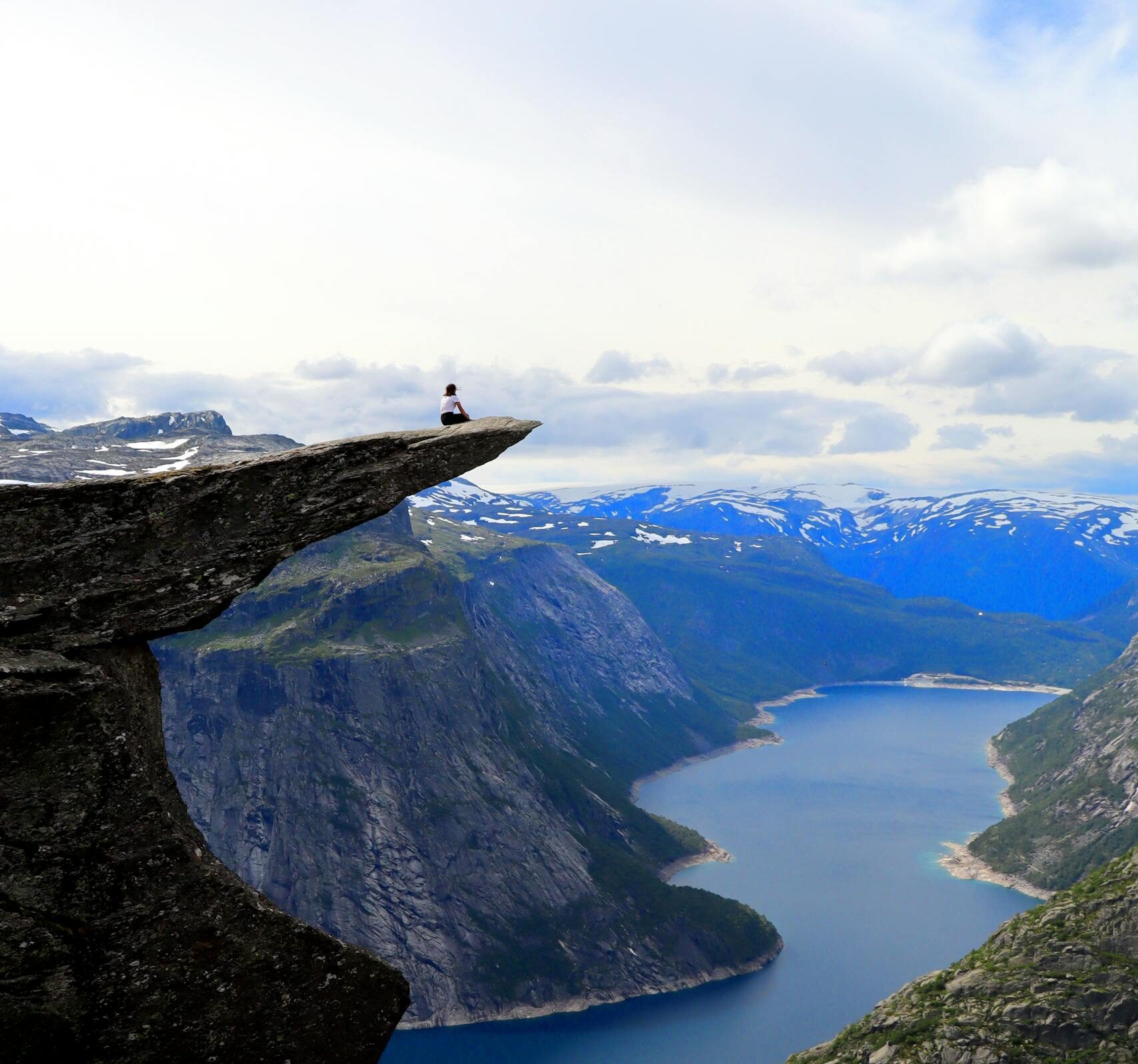 A breathtaking view from Trolltunga in Norway, overlooking a serene lake surrounded by majestic mountains.