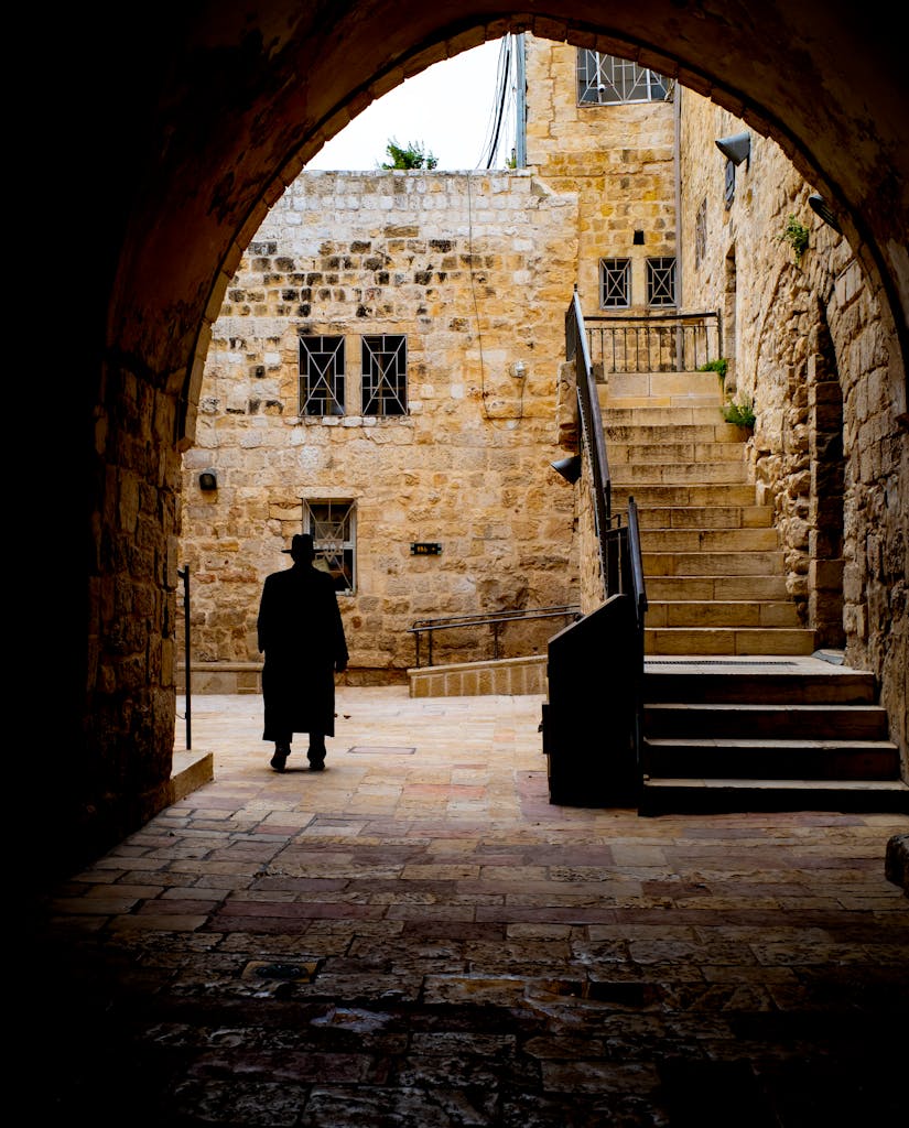 A silhouette of a person walking under an archway with ancient stone buildings in Jerusalem.