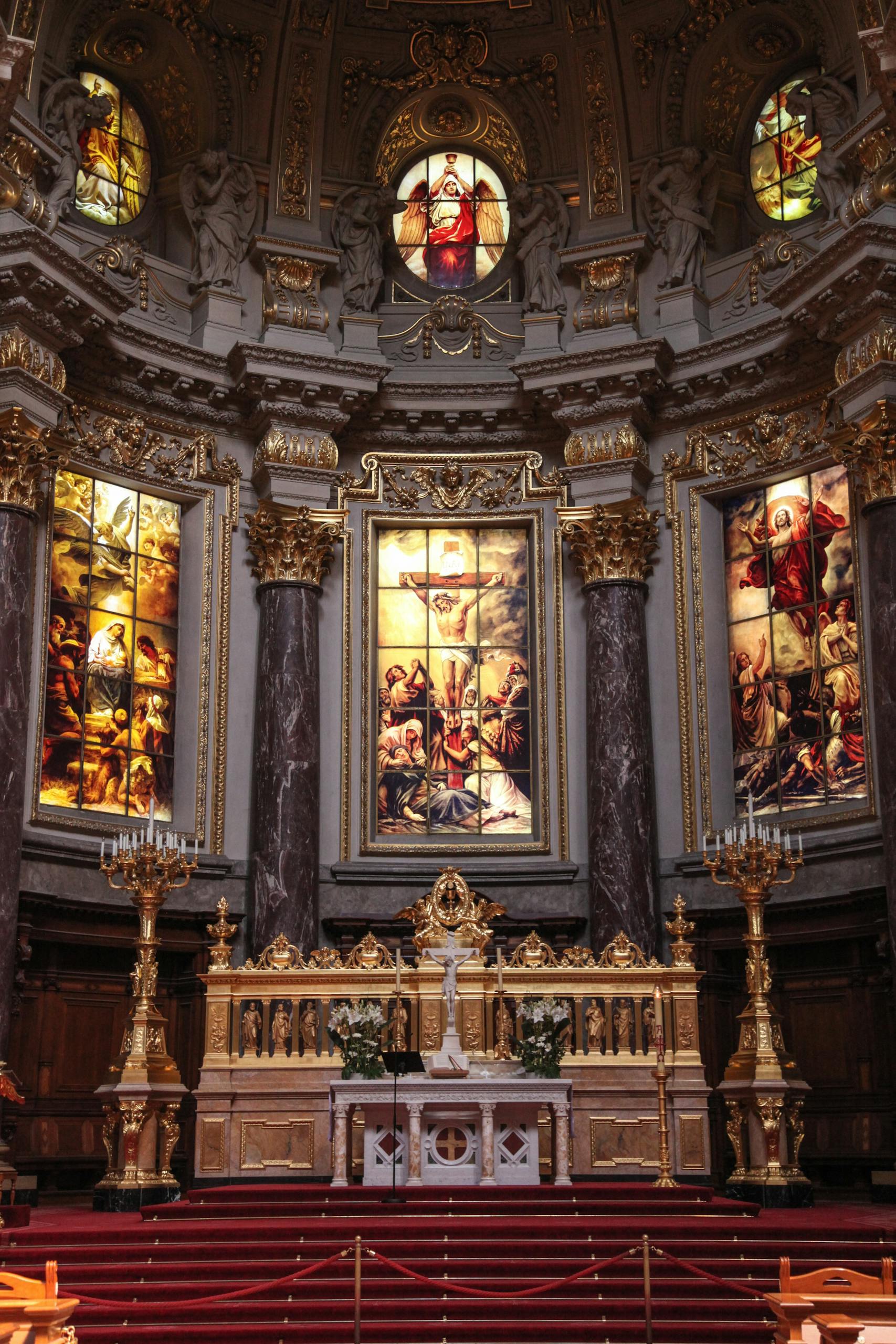 An elaborate church altar adorned with gold and intricate stained glass artwork depicting religious scenes.
