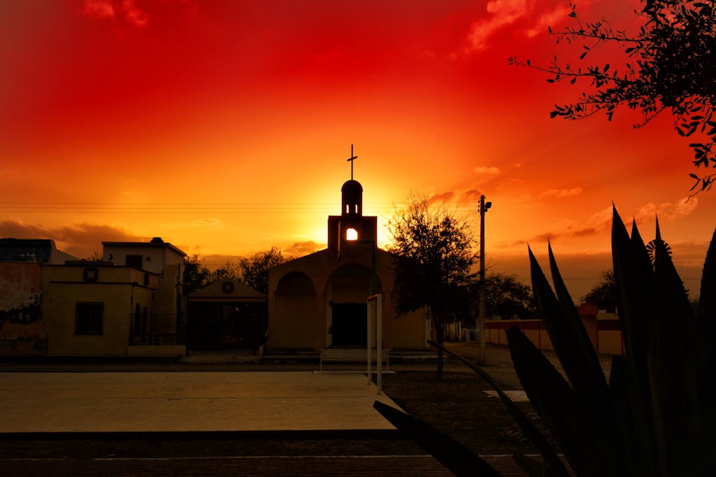 Silhouetted church with a cross against a dramatic sunset sky, showcasing vibrant colors and cultural architecture.